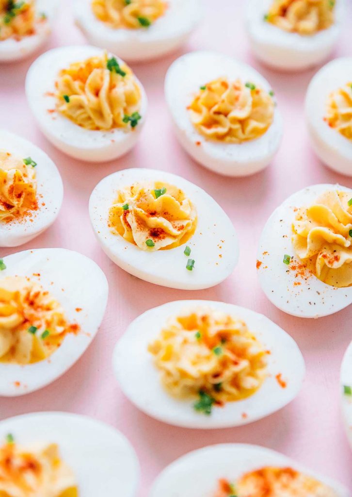 Greek yogurt deviled eggs topped with paprika and chives laid out on a pink background