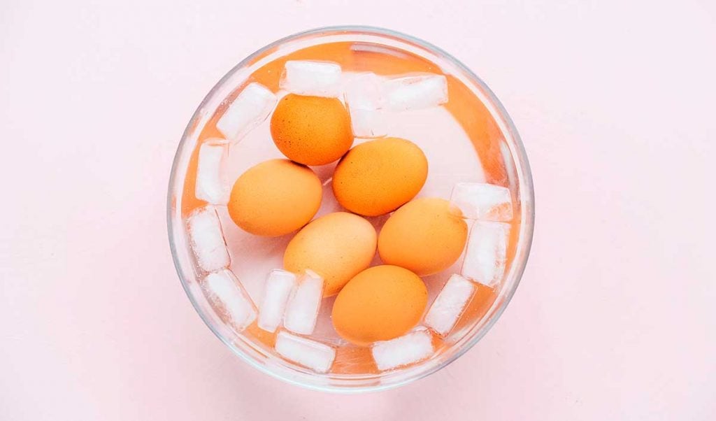Six eggs in an ice bath on a pink background