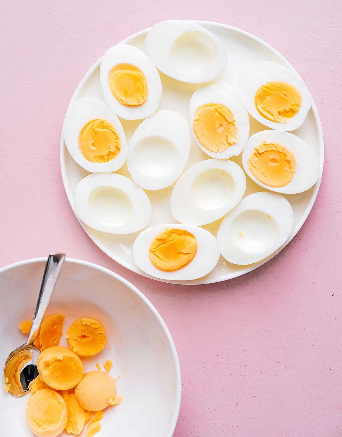 Eleven egg white halves on a plate next to a bowl of egg yolks