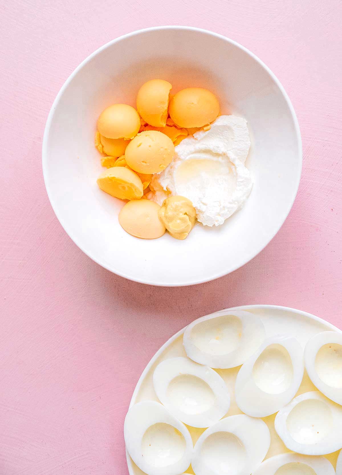 A bowl filled with egg yolks and Greek yogurt next to a plate filled with egg white halves