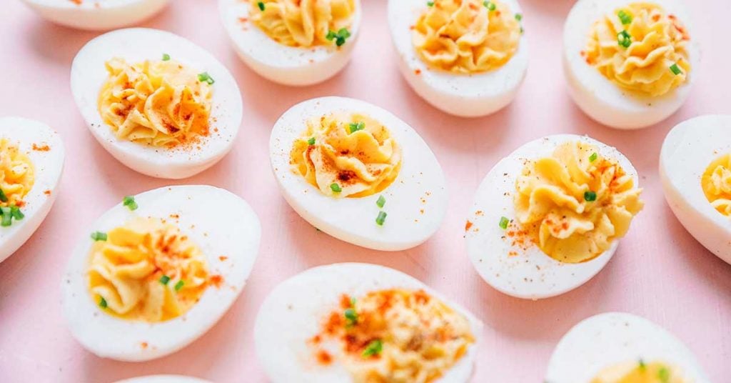 Greek yogurt deviled eggs topped with paprika and chives laid out on a pink background