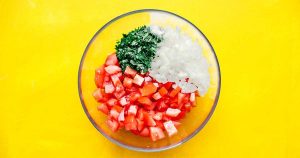 A vibrant bowl with chopped tomatoes, onions, and cilantro sits ready to accompany your huevos rancheros on a bright yellow background.