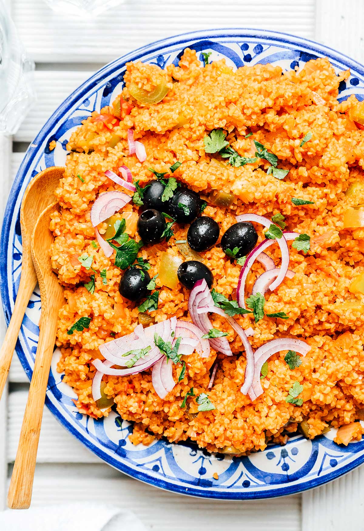 Bulgur pilaf on a plate topped with olives, red onion, and parsley.