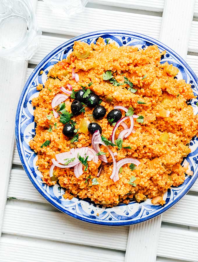 Bulgur pilaf on a plate topped with olives, red onion, and parsley.