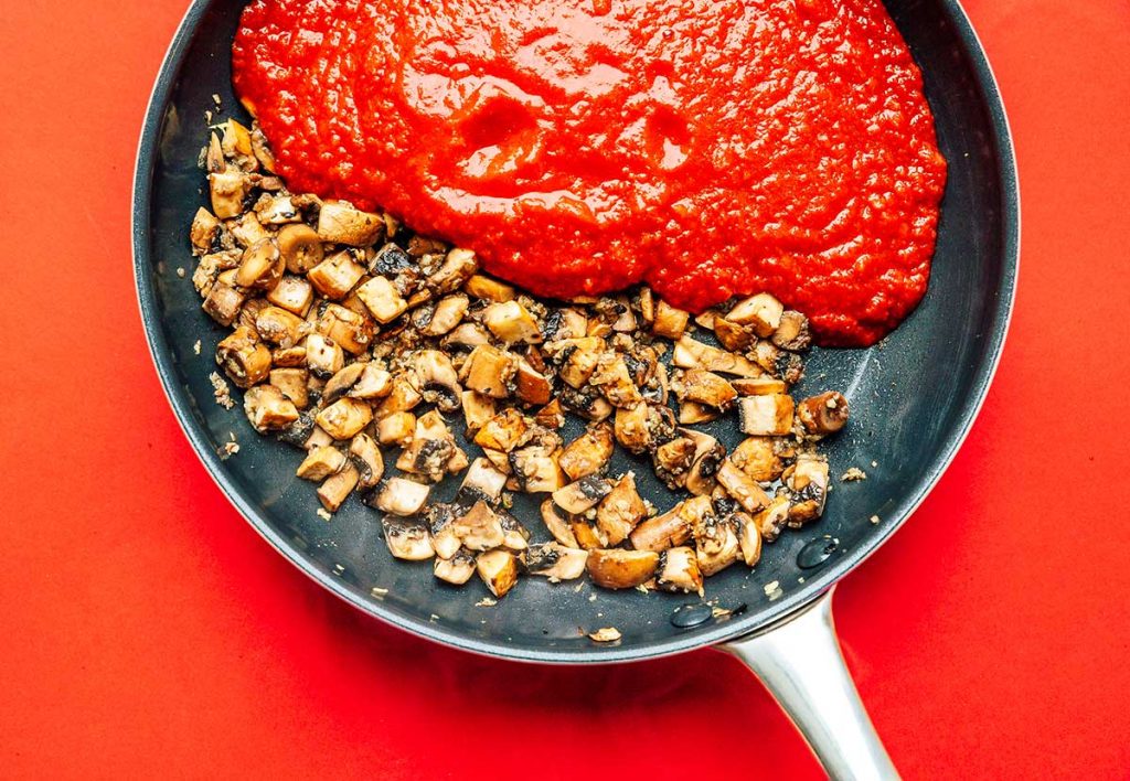 Chopped mushrooms and tomato sauce in a skillet on a red background