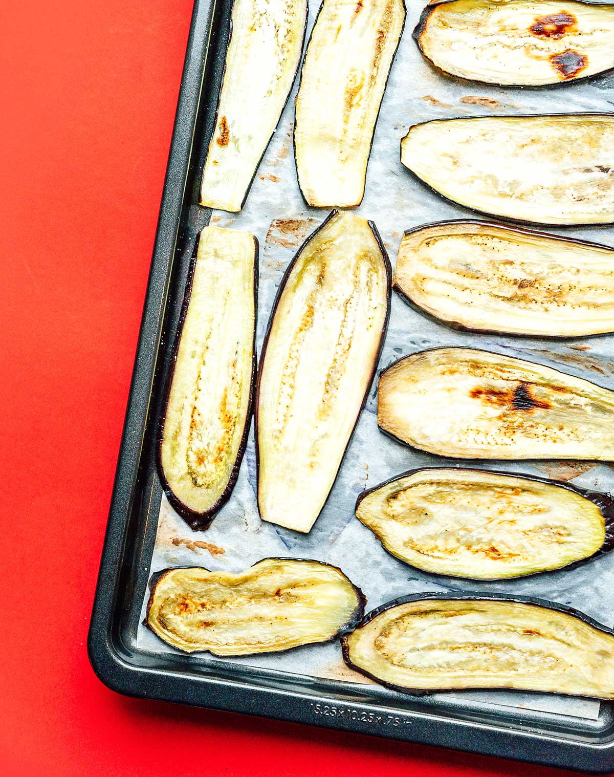 Slightly browned eggplant slices lined up in a single layer on a baking sheet 