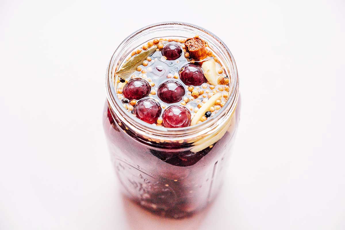A mason jar filled with pickled grapes in their spiced liquid mixture