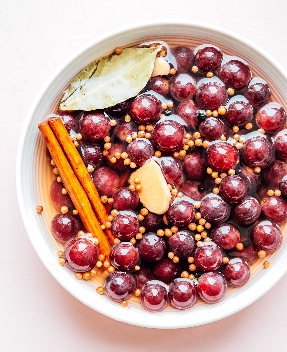 A white bowl filled with the water and vinegar mixture, red seedless grapes, and various spices