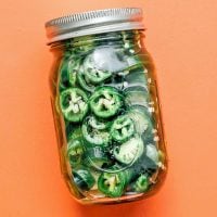 Pickles jalapenos in a jar on an orange background