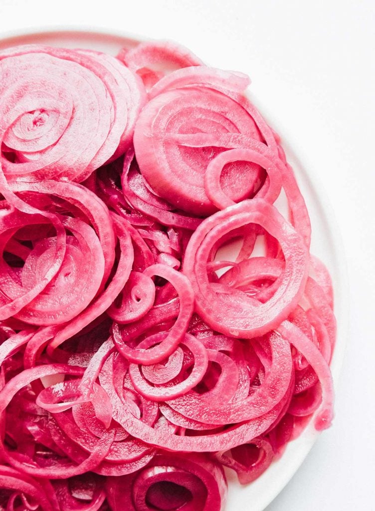 A packed pile of quick pickled red onions on a white plate on a white background