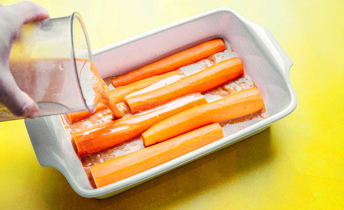 Pouring marinade over a baking dish filled with carrots 