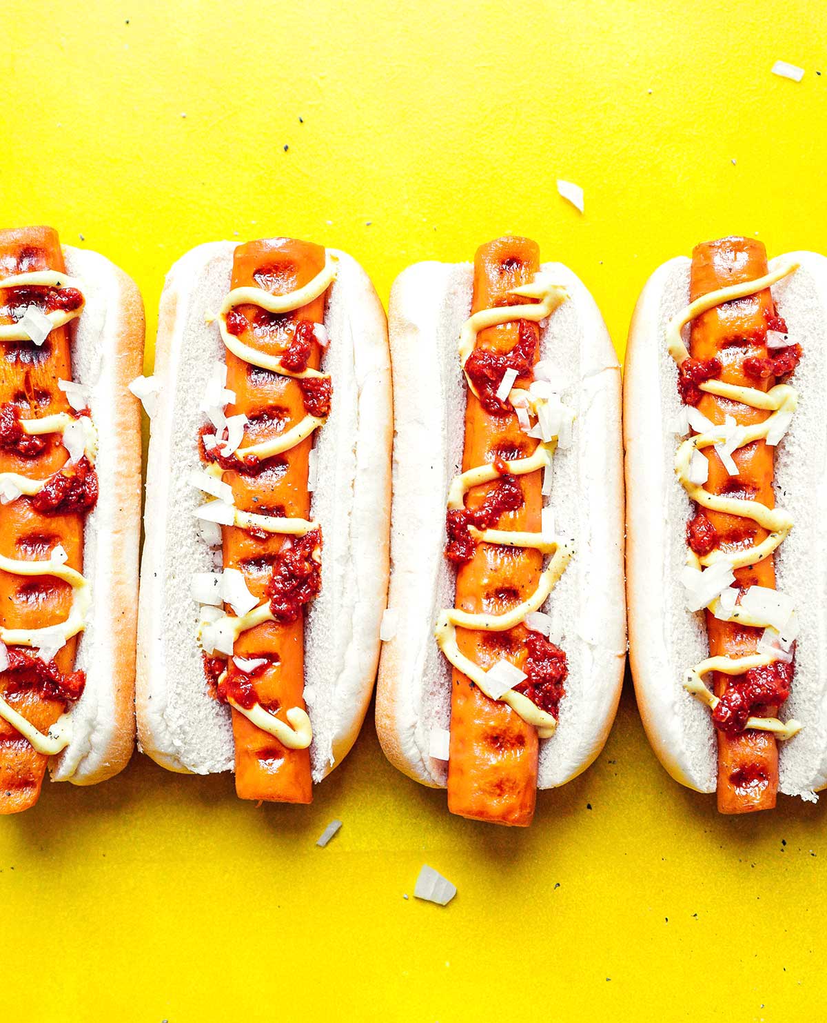 Four carrot hot dogs in buns topped with chopped white onion, ketchup, and mustard