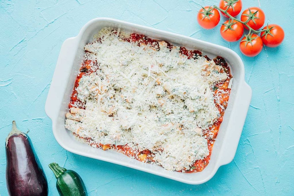 A baking dish lined with a layer of sauce, a layer of the pasta and ricotta mixture, and a layer of cheese