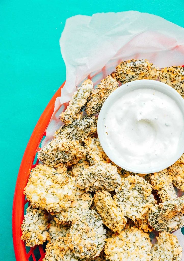 A red basket filled with air fryer fried pickles and paired with a creamy dipping sauce