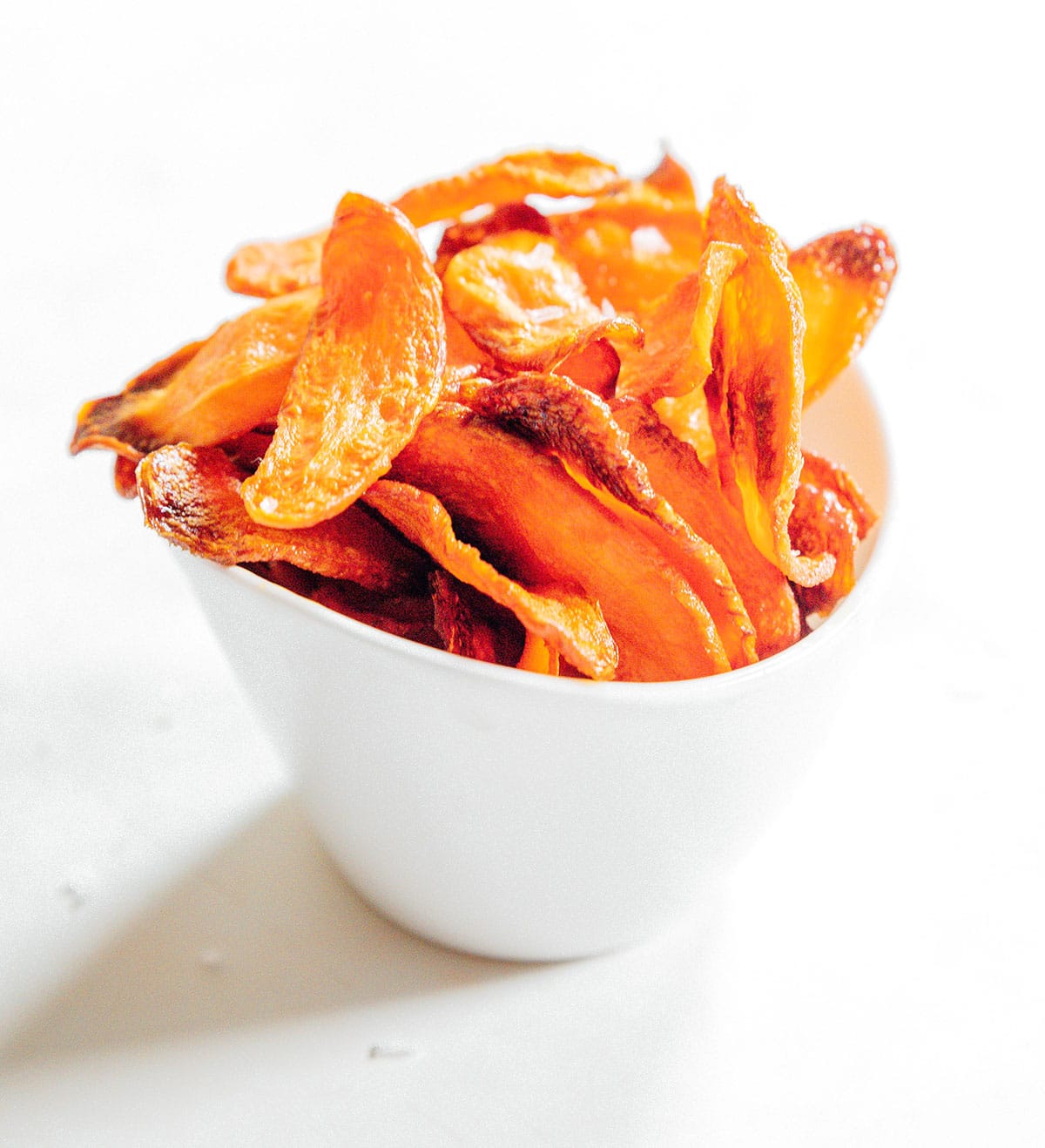 Carrot chips with flaky sea salt in a white cup.