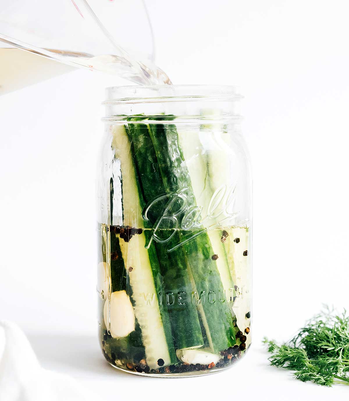 Pouring a water and vinegar mixture into a mason jar filled with cucumber wedges