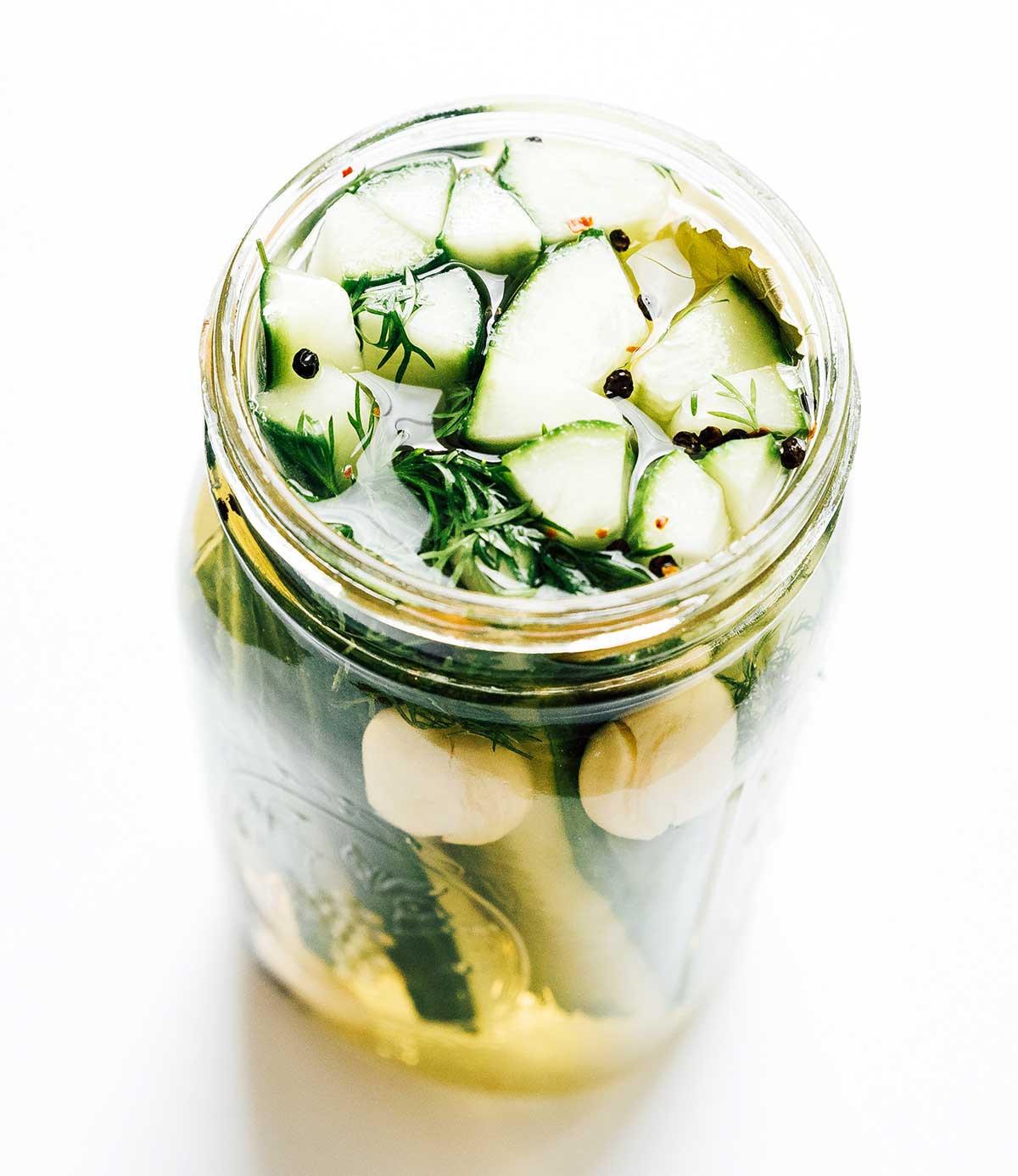 A mason jar filled with cucumber wedges, a water and vinegar pickling mixture, and various spices