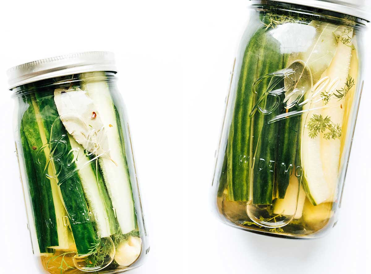 Two mason jars filled with cucumber wedges and a water and vinegar pickling mixture