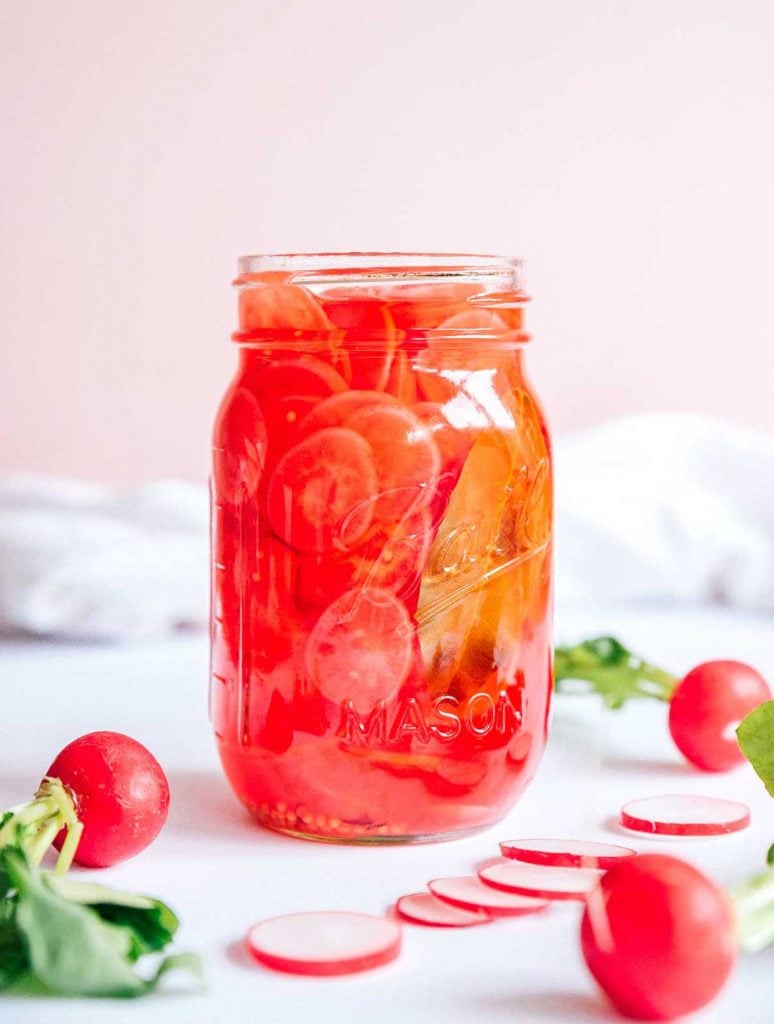 A 16-oz mason jar filled with pickled radish slices and a hot water and vinegar liquid mixture