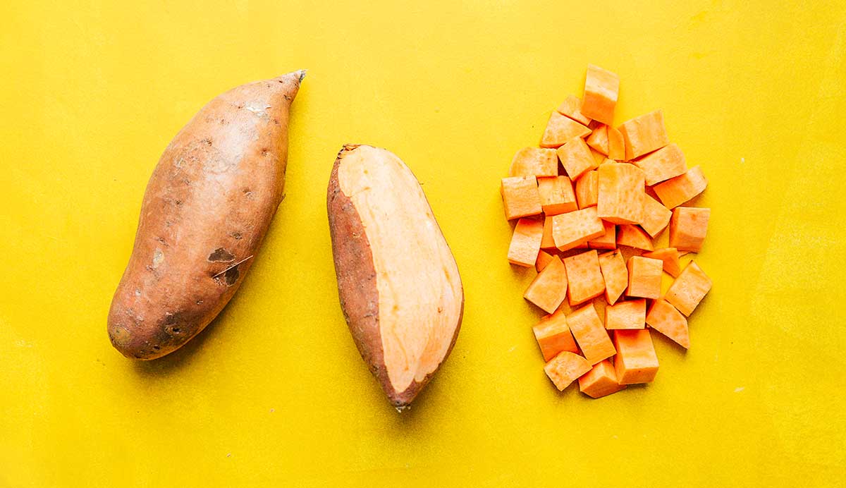 Two sweet potatoes and some cubed sweet potato pieces laid out in a row on a yellow background