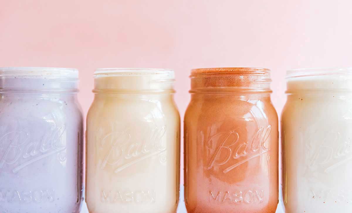 For mason jars in a row filled with different almond milk: berry, vanilla, chocolate, and sweetened