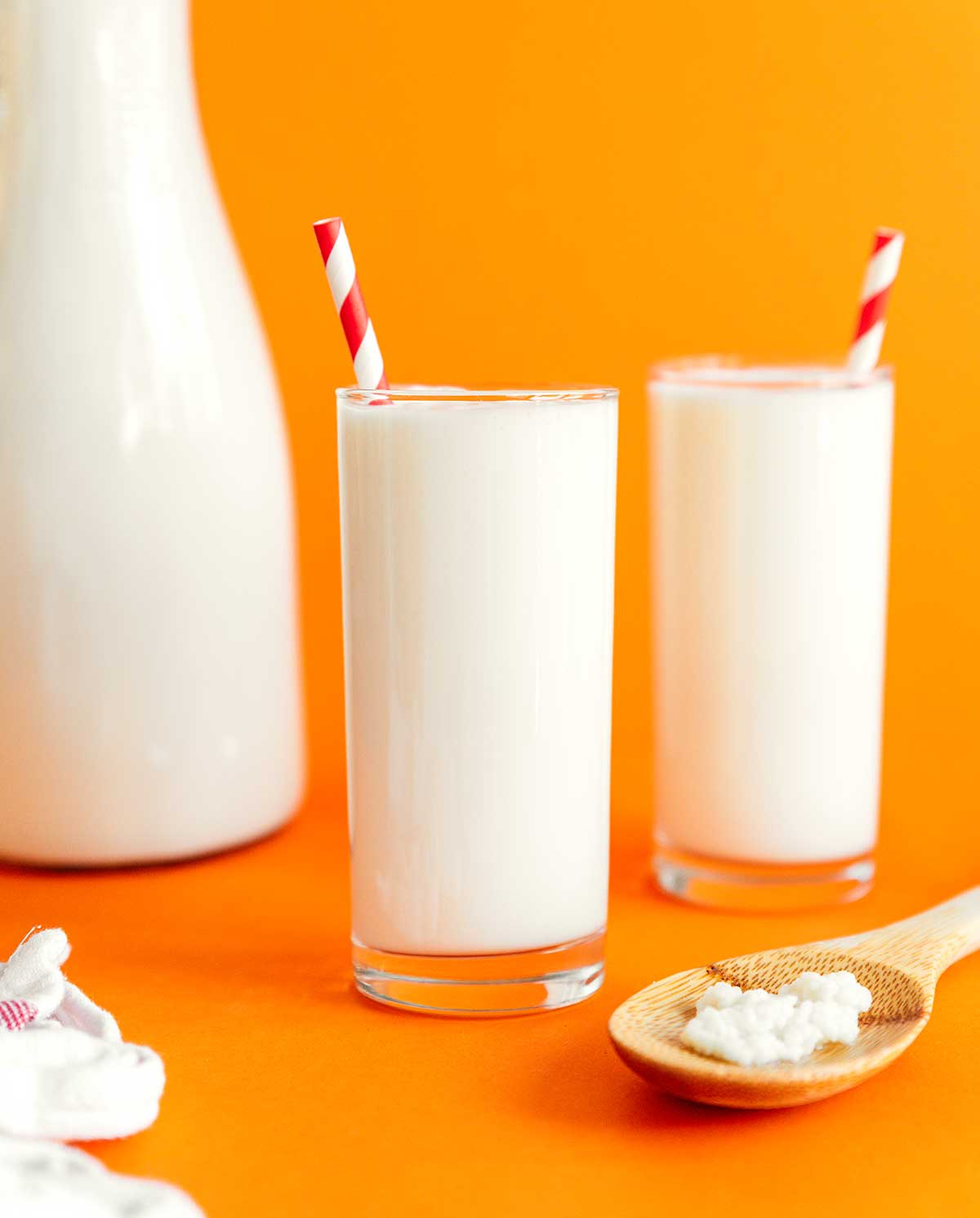 Kefir in a glass with a striped straw on an orange background
