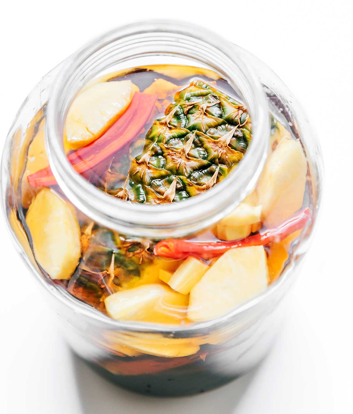 Pineapple rind, ginger, and chili in a glass jar with tepache