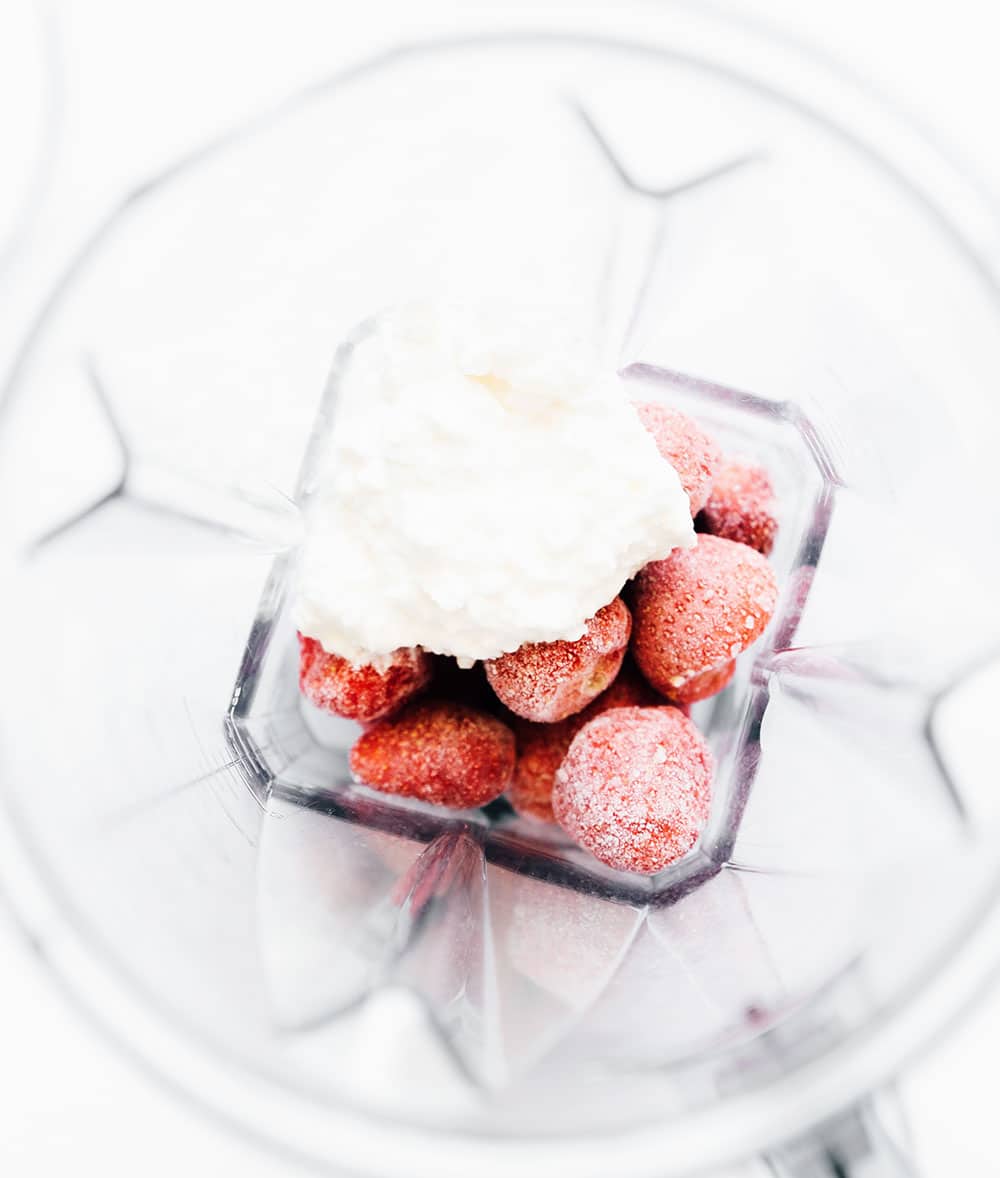 A bird's eye view of a blender filled with milk, frozen strawberries, and cottage cheese