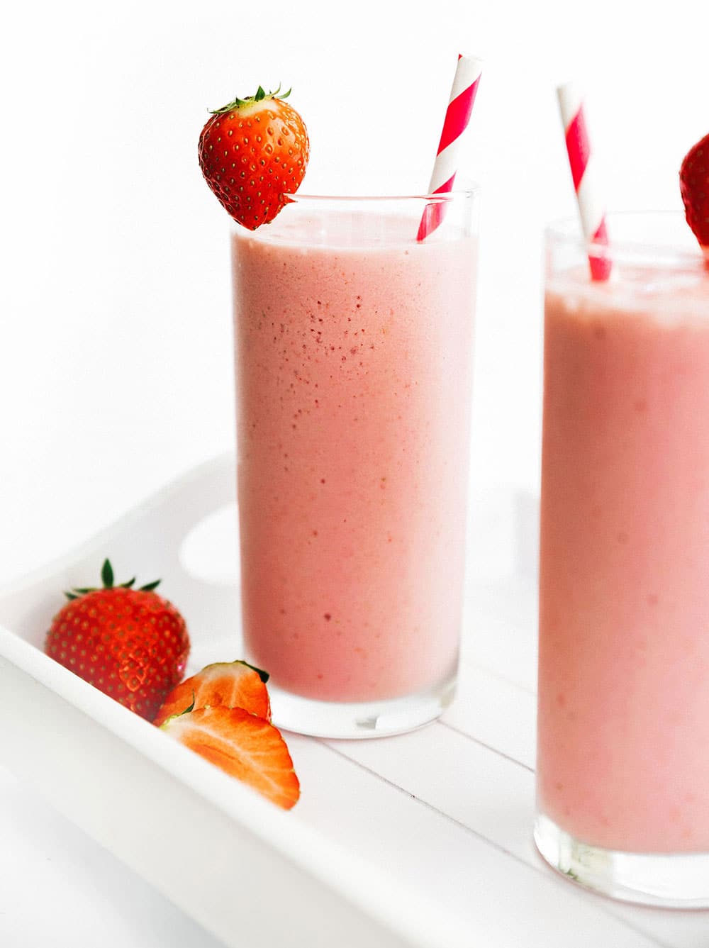 Two tall glasses filled with strawberry cottage cheese smoothies and topped with strawberries