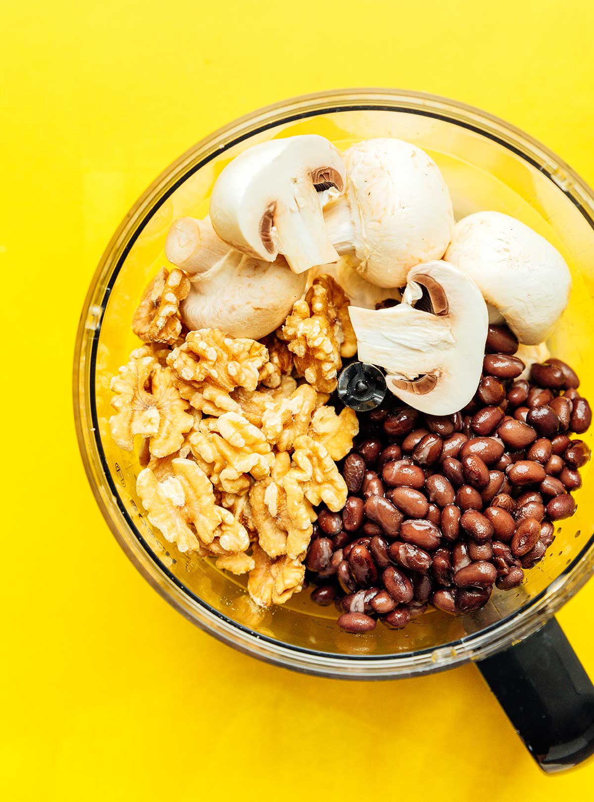 A food processor filled with black beans, walnuts, and mushrooms