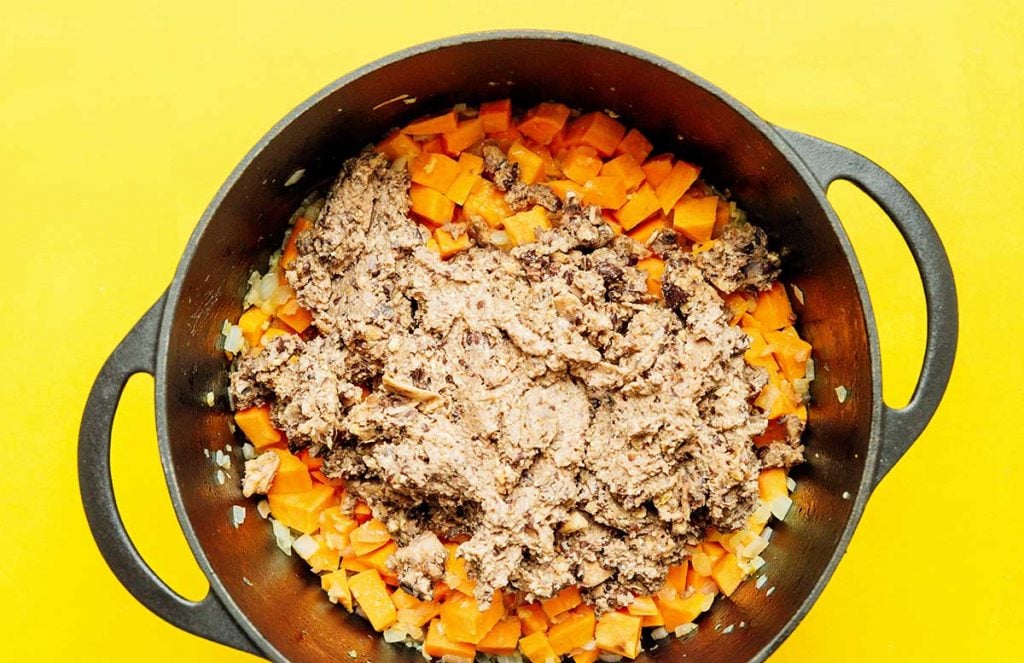 A sauce pot filled with diced sweet potato, chopped white onion, minced garlic, and black bean chili meat