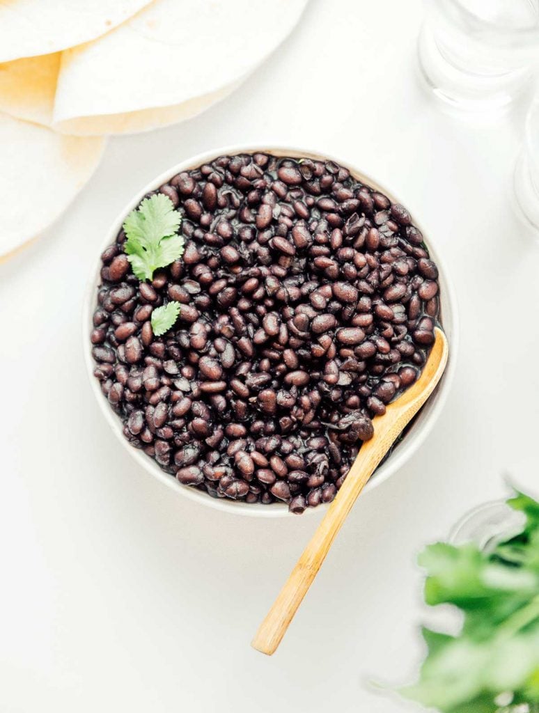 A wooden spoon placed inside a bowl filled with cooked beans