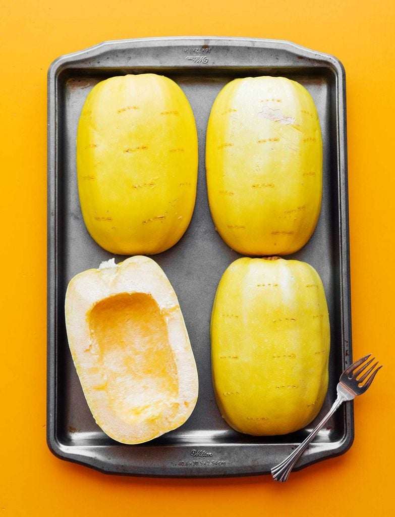 Four spaghetti squash halves laid out on a baking sheet ready to be roasted in the oven