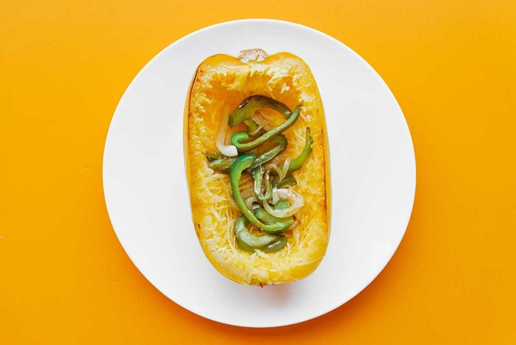 A hollowed out spaghetti squash half filled with sautéed green peppers and onions