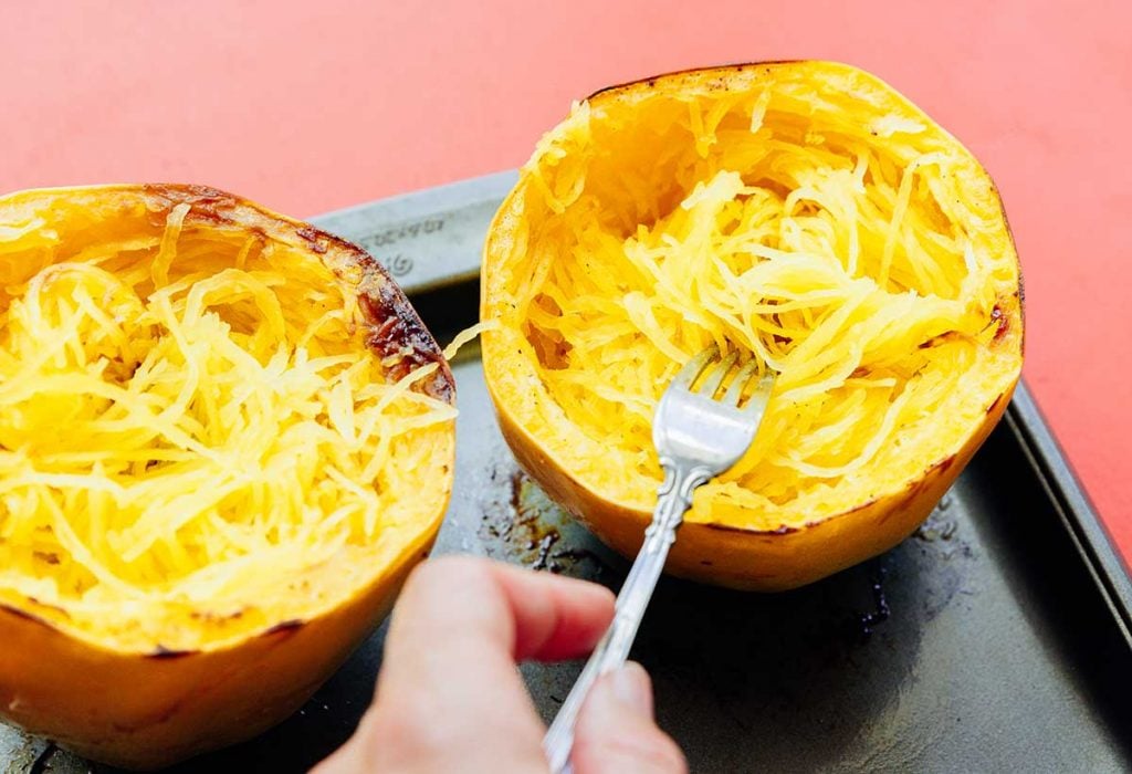 Using a fork to pull strands of the inside of a spaghetti squash, creating spaghetti-like noodles