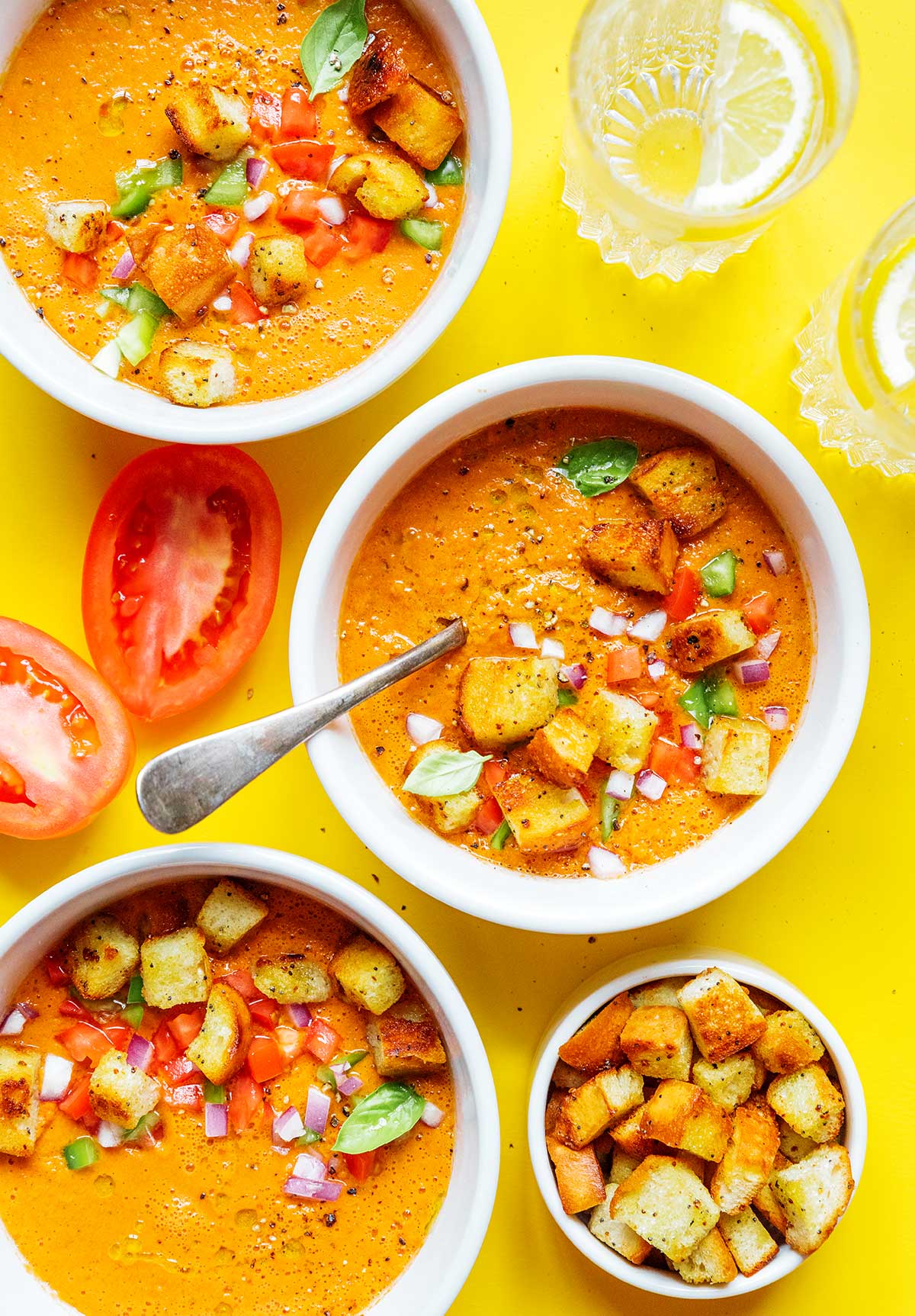 Two bowls of tomato gazpacho topped with croutons, tomatoes, green peppers, and red onion