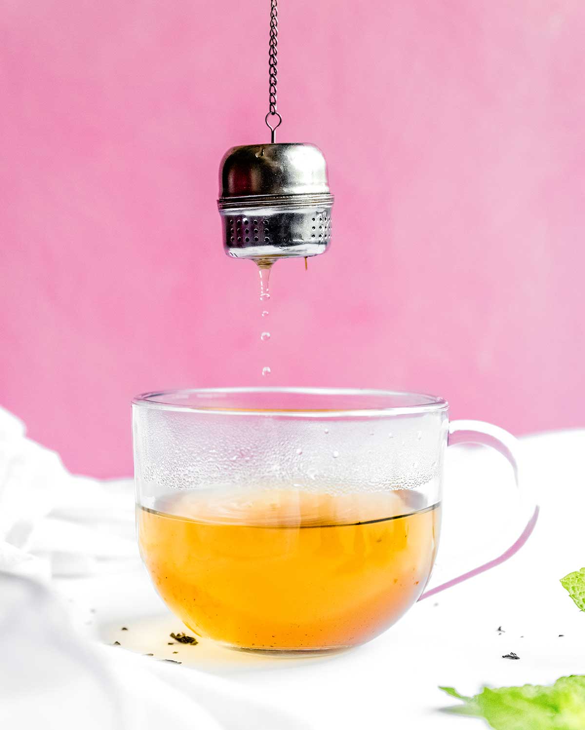 Adding loose leaf tea to a glass on a pink background