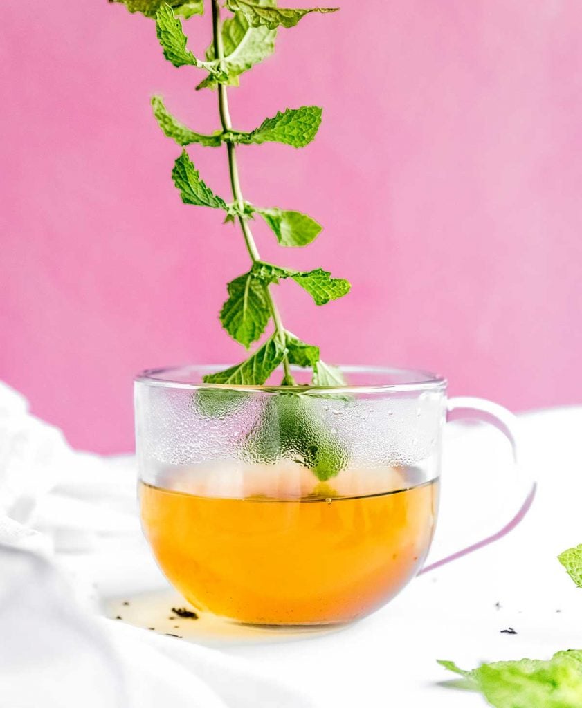 Adding mint leaf tea to a glass on a pink background
