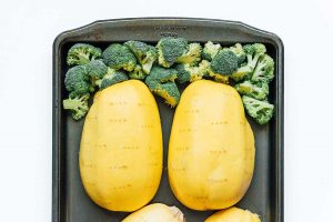 Two halved spaghetti squashes and broccoli florets on a baking sheet, ready to transform into a deliciously creamy spaghetti squash alfredo casserole.