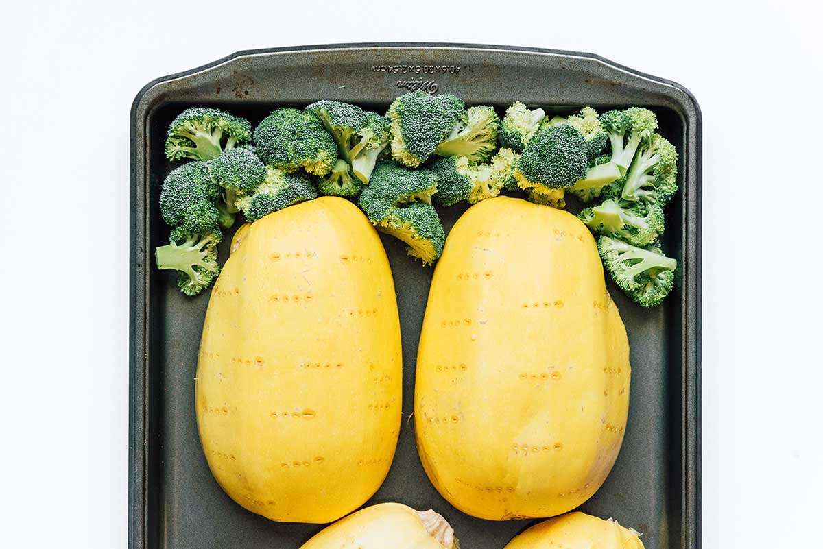 Two cups of broccoli and two spaghetti squash halves placed face-down on a baking sheet