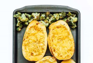 Roasted spaghetti squash halves and broccoli florets on a baking tray, perfectly prepped for a delightful twist on a classic spaghetti squash Alfredo casserole.