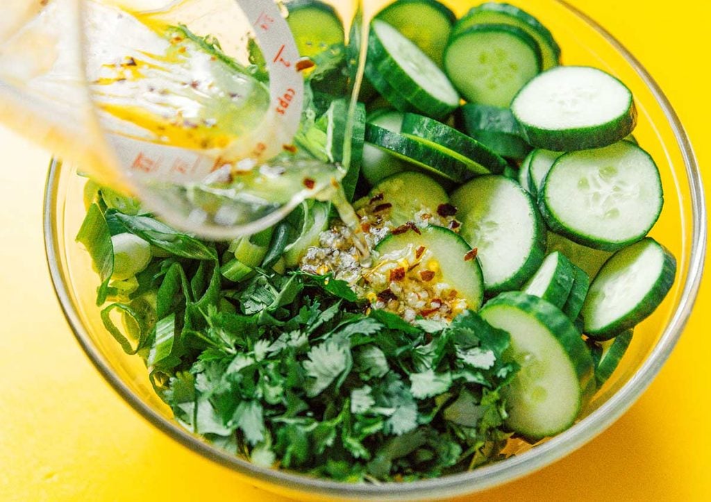Drizzle a vinegar and sesame oil dressing over a bowl filled with cucumbers, green onions, and cilantro