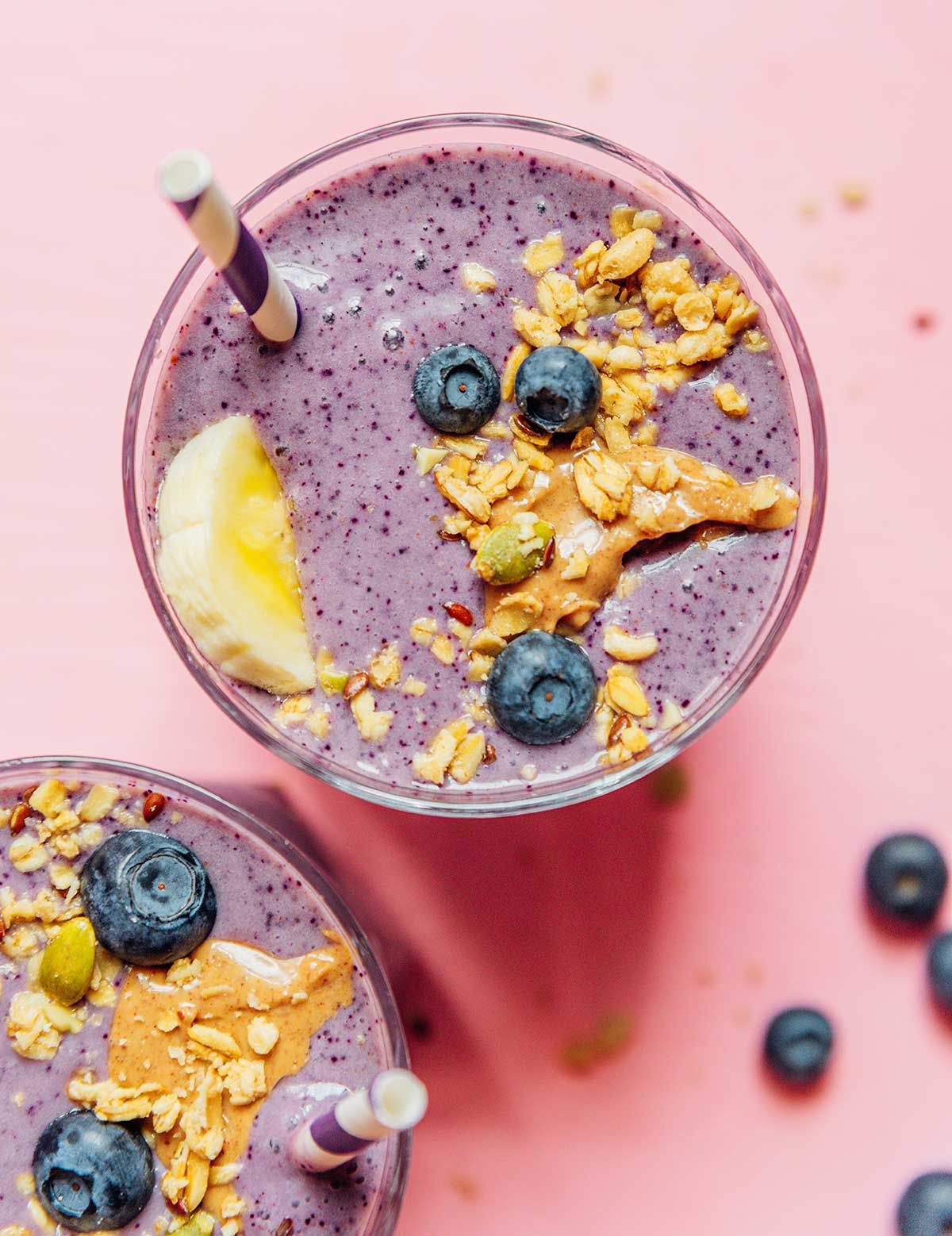 A glass filled with blueberry banana smoothie and topped with nut butter, granola, blueberries, and a banana slice