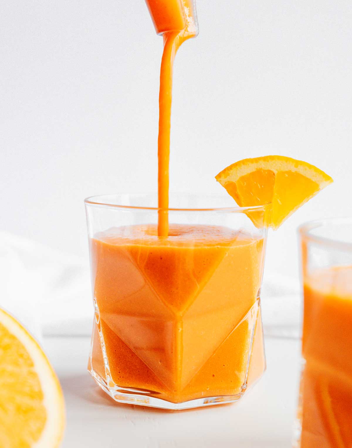 Pouring carrot smoothie with citrus and ginger from a blender into a glass