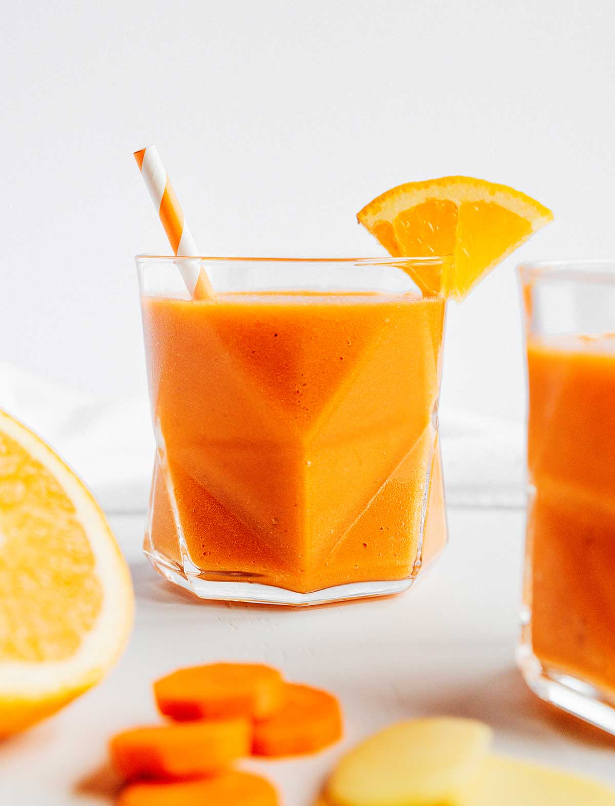 A glass filled with freshly blended carrot smoothie with citrus and ginger and decorated with an orange slice