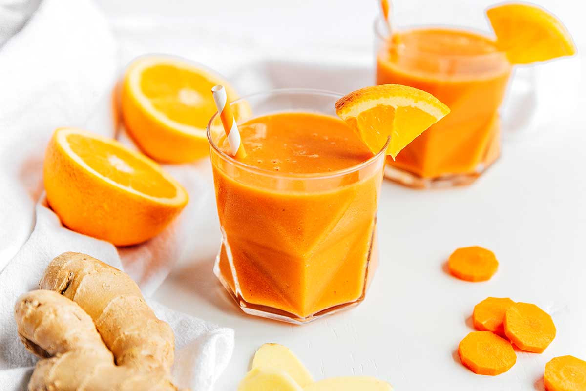 A glass filled with freshly blended carrot smoothie with citrus and ginger and decorated with an orange slice