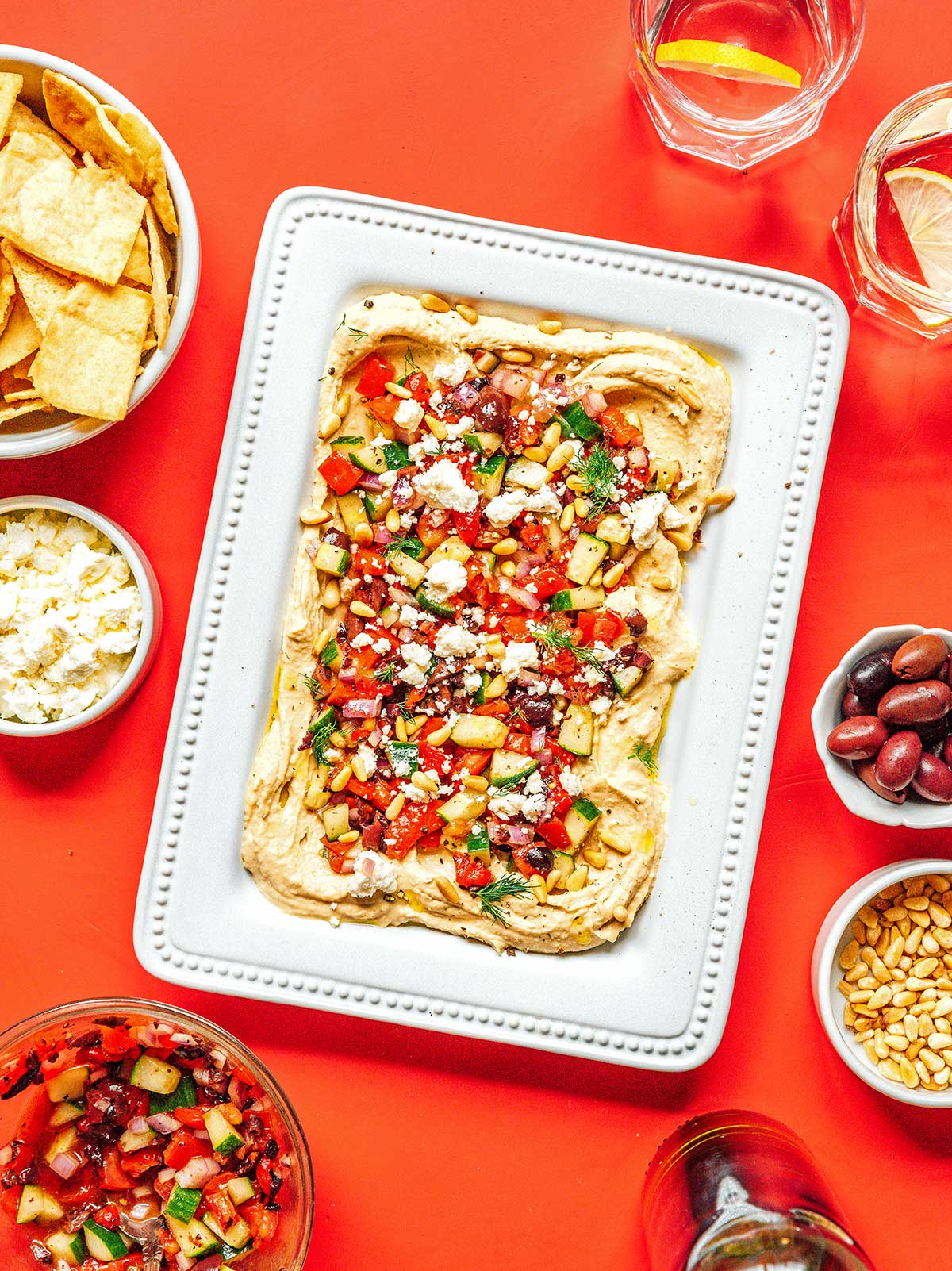A rectangular white platter filled with Mediterranean layered hummus dip