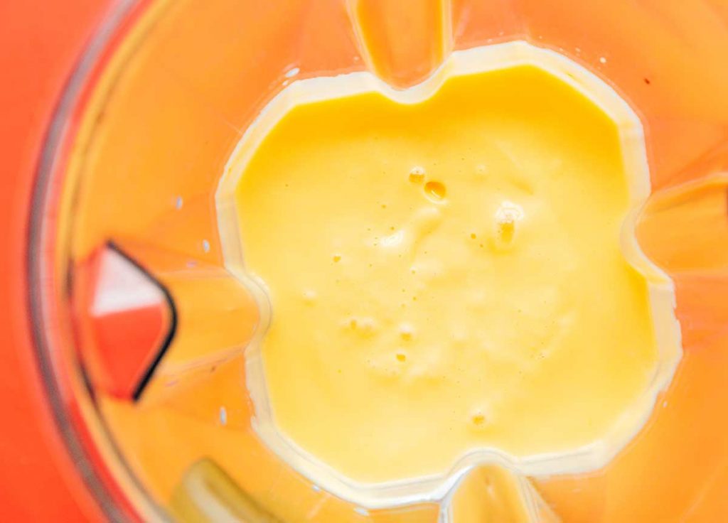 A blender filled with freshly blended mango, milk, and Greek yogurt