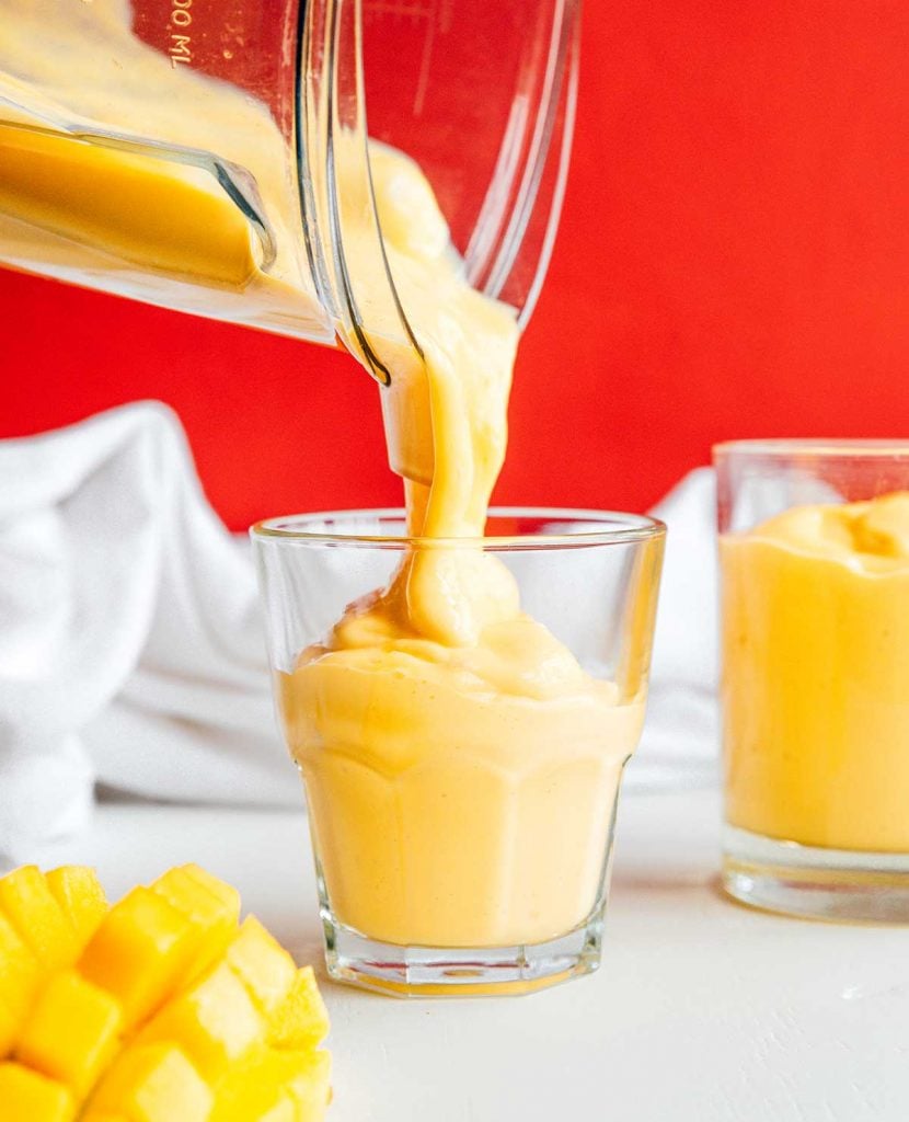 Pouring freshly blended mango smoothie from a blender into a glass