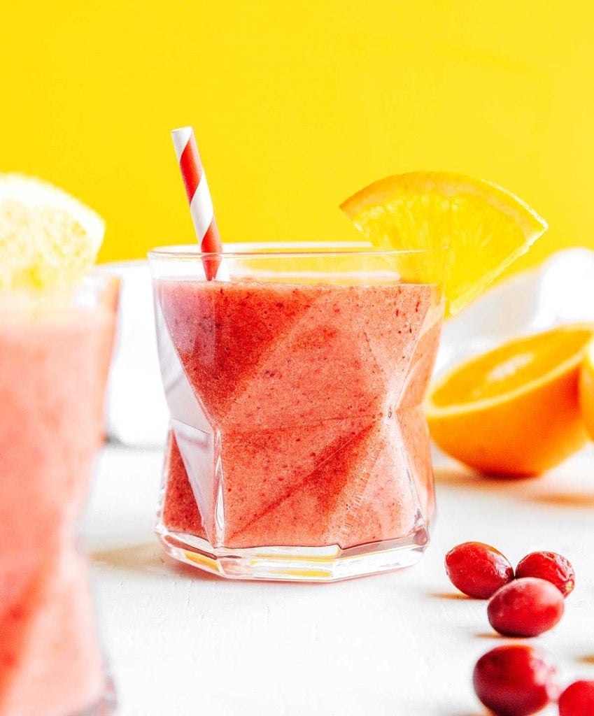 A glass filled with cranberry smoothie and decorated with an orange slice